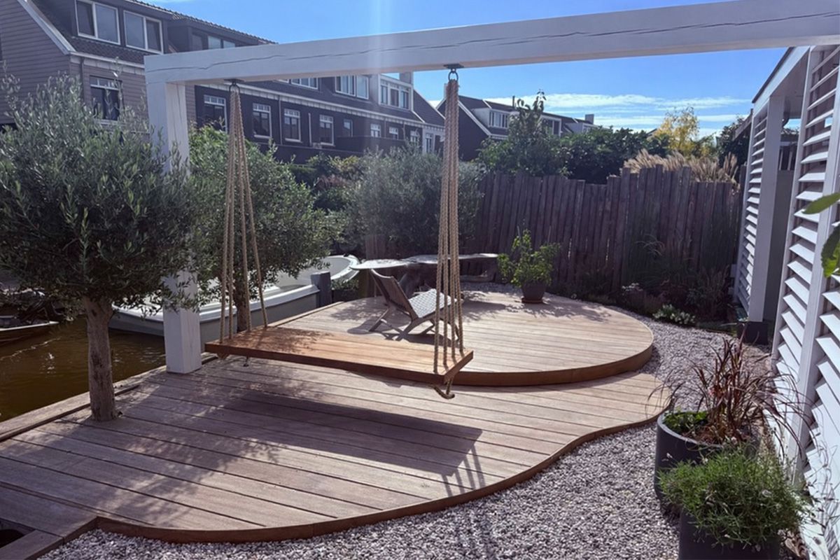 Custom outdoor living project featuring curved wooden deck with rope swing, white pergola, and landscaped garden