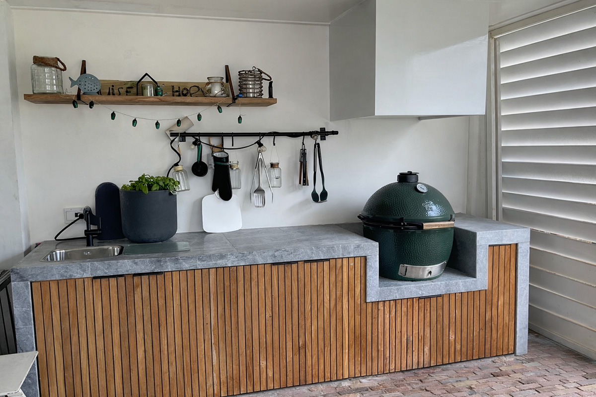 Custom outdoor kitchen project featuring concrete countertops, wooden slat cabinets, green ceramic grill, and organized hanging utensils