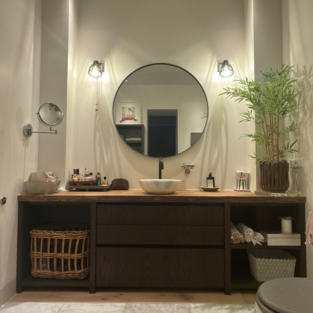 Custom bathroom vanity featuring wooden countertop, dark cabinets, round mirror, and modern lighting