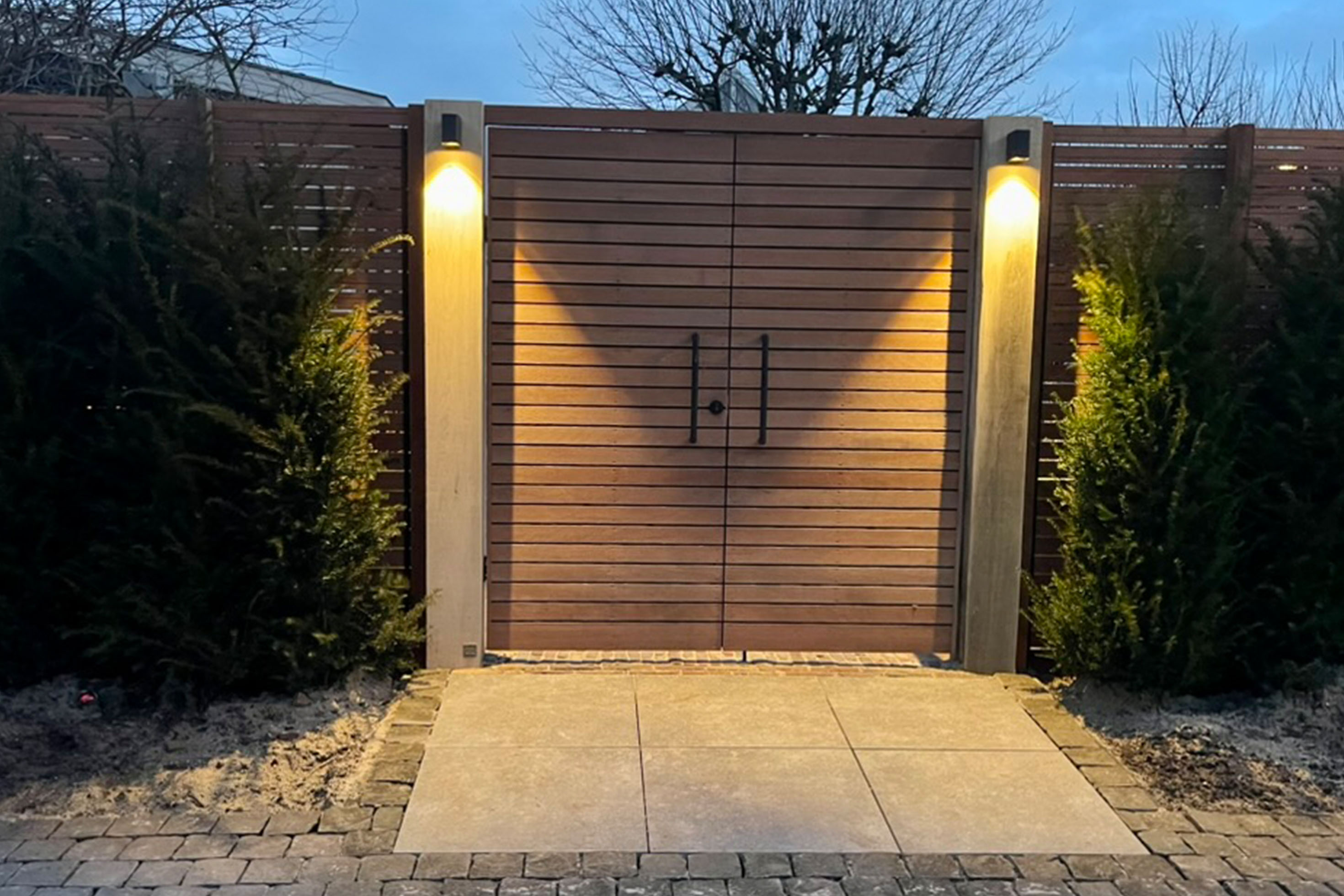 Modern wooden gate and fence with illuminated posts in custom outdoor living space