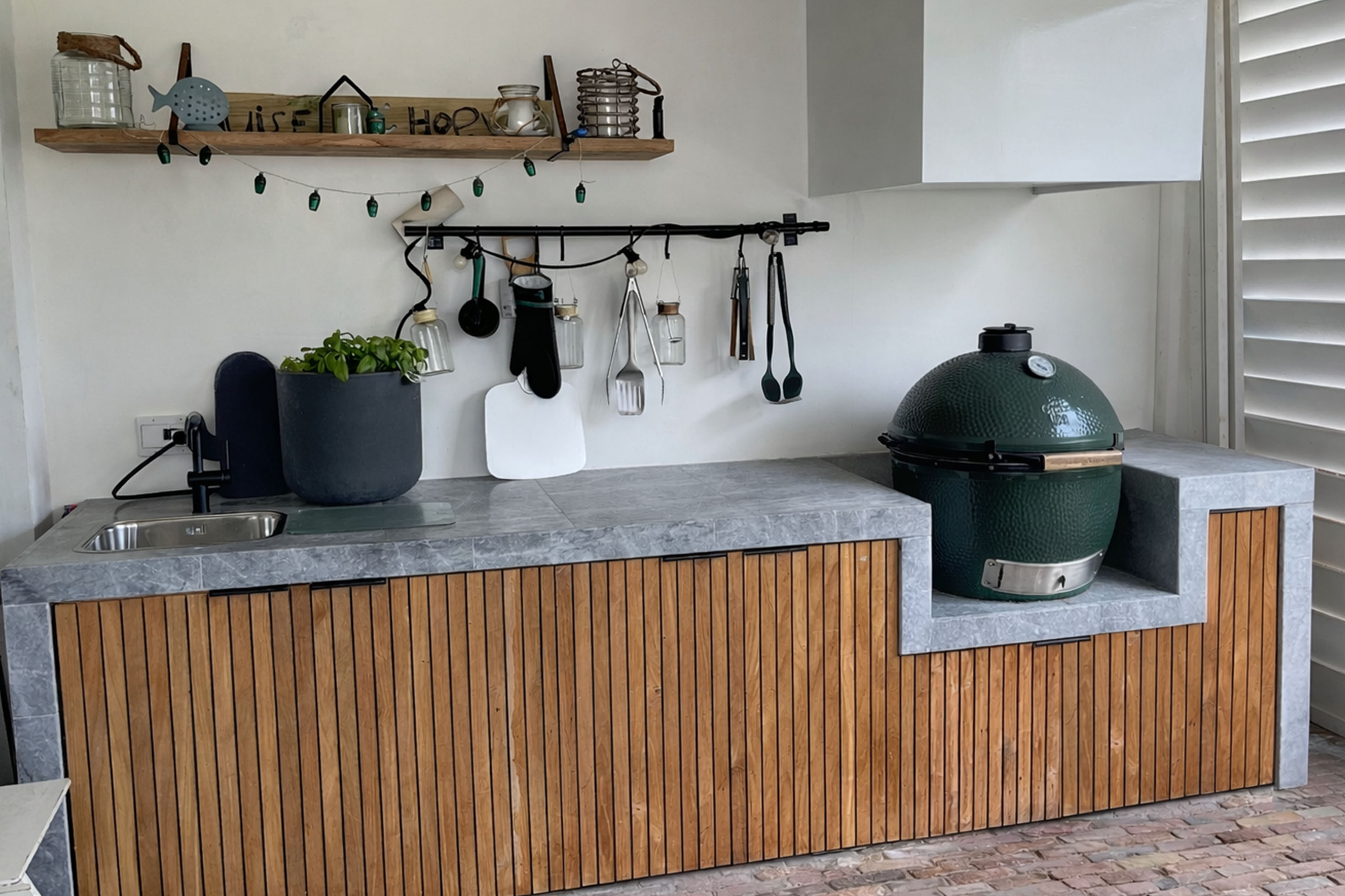Custom outdoor kitchen with wooden cabinets, stone countertop, and green ceramic grill